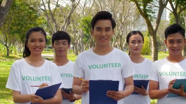 公園に5人のアジア人ボランティアが一緒に立って 手にクリップボードを持ってカメラを見て追跡する権利 — ストック動画