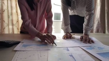 Masaüstünde duran ve üzerinde yatan çizelgeleri analiz eden iki iş kadınını kapat.