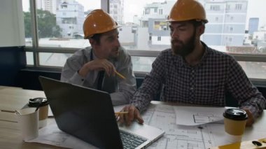 Ofiste birlikte oturan iki erkek mühendise yakınlaş, dizüstü bilgisayara bak ve planları tartış.