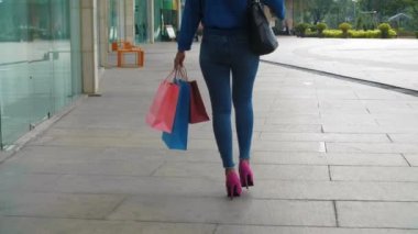 Kot pantolon giyen, pembe topuklu ayakkabı giyen, renkli çantalı, alışveriş merkezinin önünden geçen... 