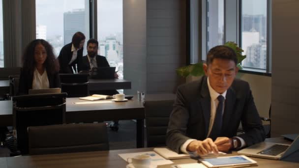 スーツとネクタイを着たアジア人ビジネスマンの手持ちPanショットタブレットで作業し オープンスペースオフィスで文書を検査 — ストック動画