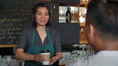 Profesyonel bayan Asyalı barmen tanınmayan erkek müşteriye kahve ikram ediyor, arkadaşça sohbet ediyor ve neşeyle gülümsüyor.