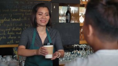 Profesyonel bayan Asyalı barmen tanınmayan erkek müşteriye kahve ikram ediyor, arkadaşça sohbet ediyor ve neşeyle gülümsüyor.