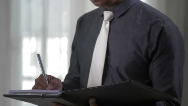 彼の手の紙でオフィスに立っているインドのビジネスマンの傾きとそれらに署名 — ストック動画