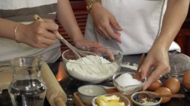 Tanınmayan kadınların elleri, klozete süzgeçten geçirilmiş unla şeker katar ve kurabiye hamuru yaparken çırpar.