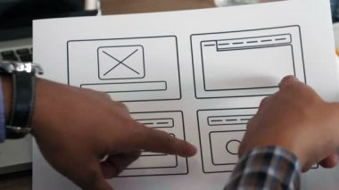 Mobil uygulama simgeleriyle kağıt tutan ve işlevselliğini tartışan tanınmayan erkek UX tasarımcılarının yakın plan görüntüsü 