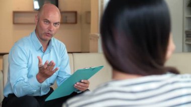 Deneyimli orta yaşlı beyaz erkek psikoloğu durumu hakkında tanımlanamayan sorular soruyor ve not alıyor.   