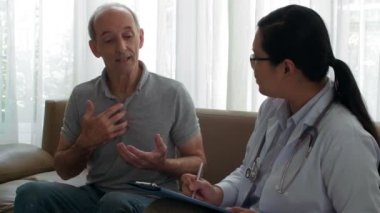 Orta yaşlı Asyalı bir adamın kanepeye oturup, onu dinlerken ve panoya yazı yazarken dikkatli bir kadın doktorla konuşması.