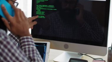 Hintli bir adamın bilgisayar ekranının önünde oturmasını, telefonla konuşmasını, sonra kaldırmasını ve kodlamaya başlamasını.
