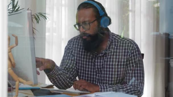 中等比例的印度胡子男子坐在电脑前 阅读一些信息 然后在笔记本上记笔记 — 图库视频影像