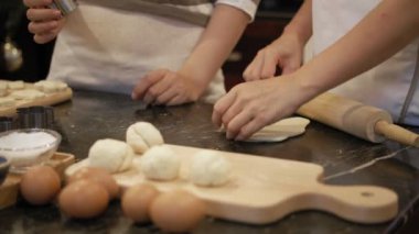 Mutfak masasında kurabiye hamuru yuvarlayan tanınmayan bir kadının yakın plan görüntüsü. Bir diğeri de kesiciyle kurabiye kesiyor.