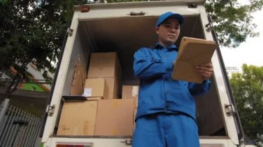 Mavi üniformalı Asyalı kuryenin elinde tabletle bilgi ararken görüntüsü düşük açılı. Sonra da gerekli kutuyu alıp ortadan kayboluyor.