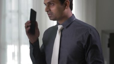 Hintli işadamının elinde telefonla ofiste dikilip iş ortağıyla telefon görüşmesi yapması.