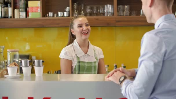Zamknięcie Młodej Kelnerki Stojącej Przy Ladzie Rozmawiającej Męskim Klientem Pomagającej — Wideo stockowe