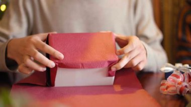 Masada oturup, pembe kağıtlı kız arkadaşına Noel hediyesi paketleyen tanınmamış bir adamın yakın plan görüntüsü.
