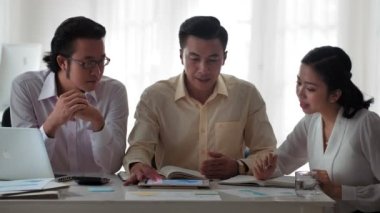 Üç genç Asyalı iş adamının ofisinde oturmuş toplantıda projeyi tartışırken orta boy fotoğrafı.