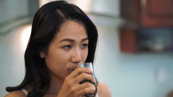 年轻漂亮的亚洲女人在家里喝着新鲜榨青菜汁 抚平头发 开开开心心地笑着 — 图库视频影像