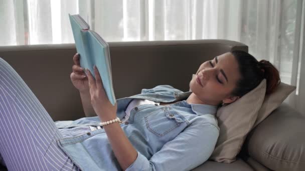 アジアの女性の中出しソファに横たわって本を読む — ストック動画