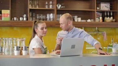 Tezgahta duran genç adam ve kadının orta boy görüntüsü. Laptop ekranına bakıyor ve kahvenin geleceğini tartışıyorlar.