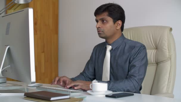 印度商人坐在电脑屏幕前的桌前 在键盘上打字 喝咖啡 — 图库视频影像