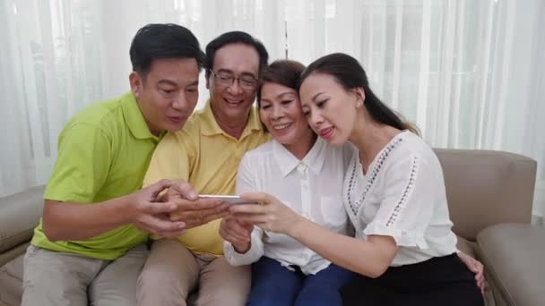 四个亚洲人坐在沙发上 兴高采烈地看着智能手机屏幕的中景照片 — 图库视频影像
