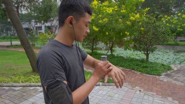 Panning Asian Man Standing Park Setting His Smart Watch Jogging — Stock Video