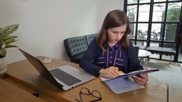 中等比例的年轻女商人坐在办公桌前 一边用笔记本电脑键盘打字 一边看图表 一边继续打字 — 图库视频影像