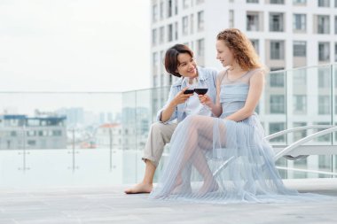 Çok ırklı güzel lezbiyen çift şarap içip çatıda sohbet ediyorlar.