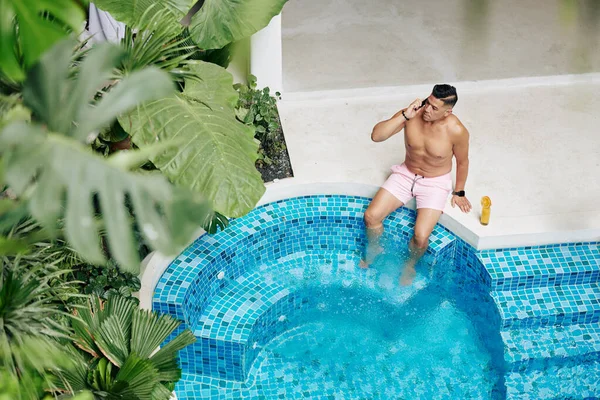 水泳プールで深刻なフィット男日光浴 オレンジジュースを飲み 電話で話す — ストック写真