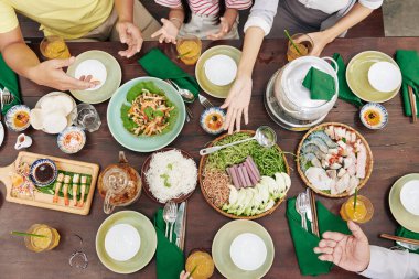 Yemek masasında yemek yiyen ve tartışan aile üyelerinin elleri, yukarıdan manzara