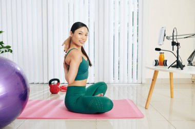 Oldukça formda Asyalı bir kadın blogu için fitness videosu çekerken elini arkasını sıkarak ineklere poz veriyor.