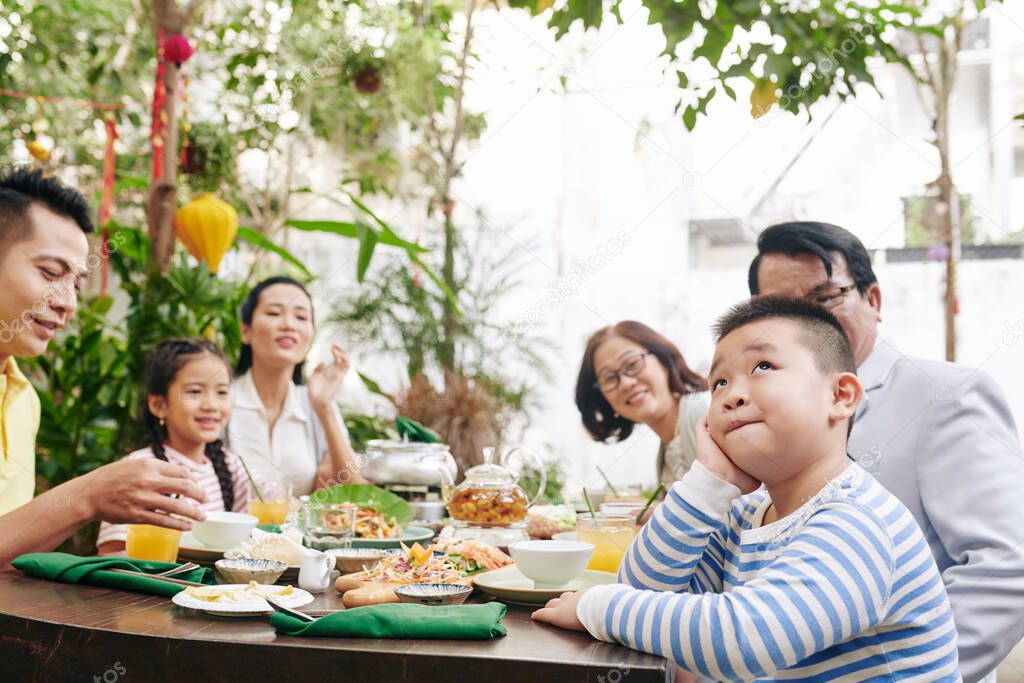 Family looking at adorable pensive little boy sitting at dinner table