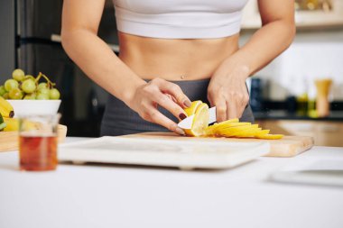 Sıska bir kadının sağlıklı kahvaltı yaparken sulu limon keserken ya da mutfak tezgahında akşam yemeği pişirirken yakın plan görüntüsü.