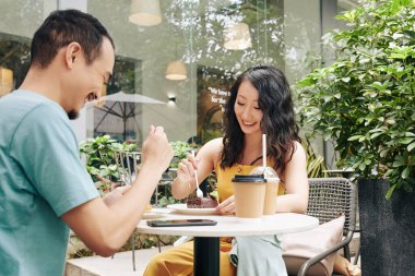 Açık kafede romantik bir buluşma yaşarken kahve içip tatlı yiyen mutlu genç Çinli çift.