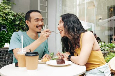 Kafe masasında otururken kız arkadaşını pastayla besleyen mutlu genç adam.