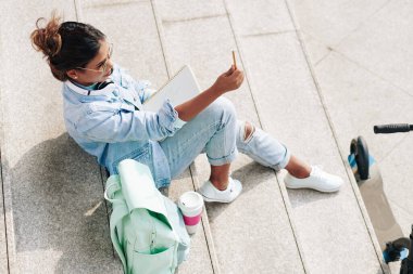 Adımlarda oturan kadın sanatçı, uzaktaki objeyi ölçmek için elini kalemle kıs ve uzat.