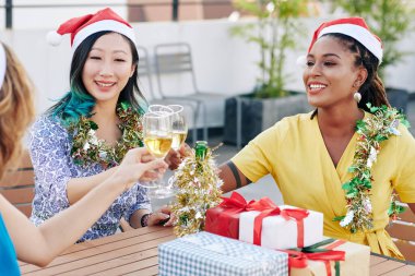 Noel Baba şapkalı, şampanya içen ve Noel partisinde hediyeleşen çok ırklı genç kadınlardan oluşan bir grup.