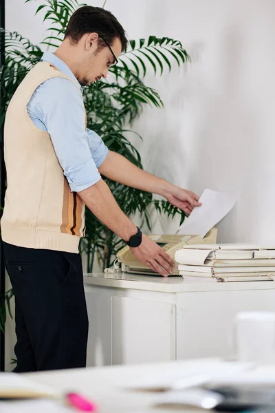 Young businessman in glasses printing out important document or report or sending fax