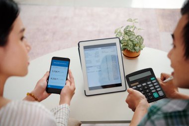 Genç çift yatırım hesaplarını masa bilgisayarından kontrol ediyor ve hangi hisseleri almaları gerektiğini tartışıyor.