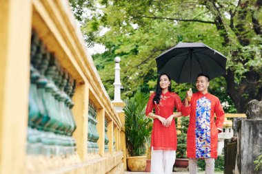 Geleneksel elbiseli, gülümseyen Vietnamlı güzel bir çift şemsiyeyle parkta yürüyor ve bahar festivalini kutluyor.