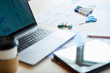 Ofis masasında açılan dizüstü bilgisayar, çizelgeler, işaretleyiciler ve klasör klipleri, seçici odaklanma