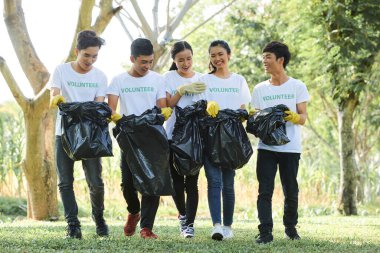 Gönüllü olarak parktan topladıkları çöp torbalarını taşıyan neşeli Asyalı genç insanlar.