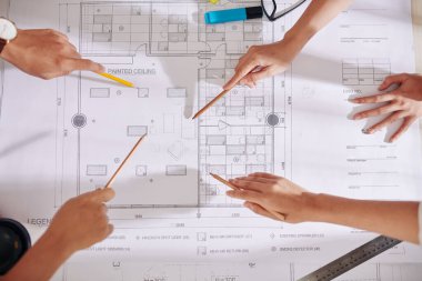 Mimarlar ve tasarımcıların elleri gelecek iç tasarım projesini tartışırken masadaki planlara işaret ediyor