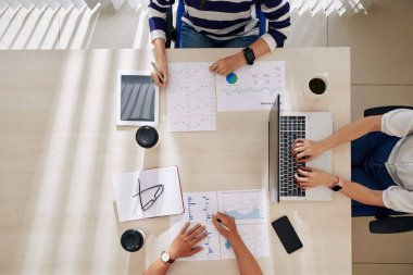 Genç iş adamları ofis masasında oturup dizüstü bilgisayarlar üzerinde çalışıyor ve mali istatistikleri inceliyor, yukarıdan bakıyorlar