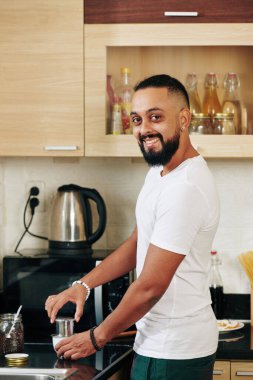 Portrait of happy bearded young man using Vietnamese coffee press when making morning beverage