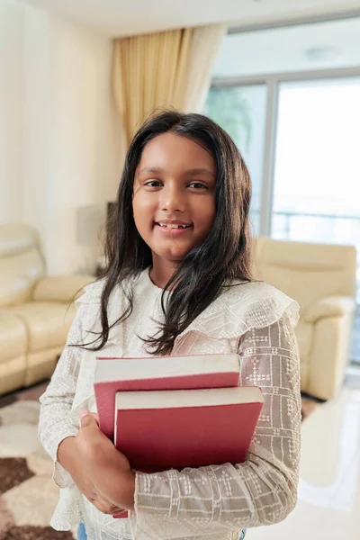 兴高采烈的印度少女站在公寓里举着书本 对着相机笑 — 图库照片