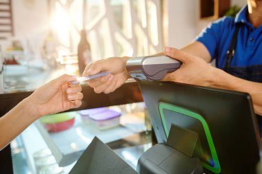 Kahve dükkanında kahve parasını öderken kredi kartı kullanan kadın müşterilerin elleri.