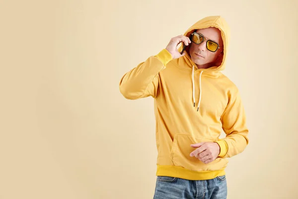 Sarı Kapüşonlu Güneş Gözlüklü Bir Adamın Stüdyo Portresi Telefonda Arkadaşıyla — Stok fotoğraf