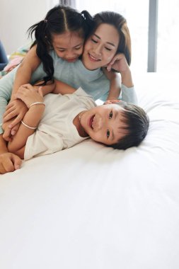 Mutlu küçük Asyalı çocuk anne ve kız kardeşiyle oynayıp kameraya bakıyor.