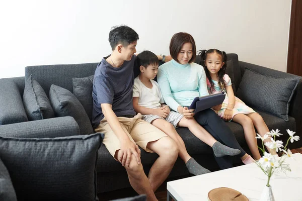 ベトナム人の家族2人の子供がソファで休み タブレットコンピュータでアプリを使用して夏休みを計画しています — ストック写真